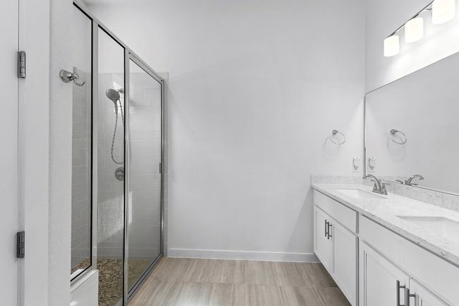 Bathroom featuring a tile shower, double vanity, and baseboards | Image 23
