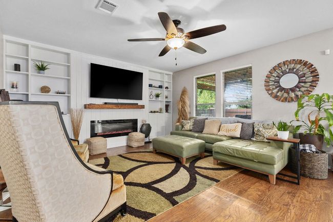 Living room with ceiling fan, built in shelves, wood finished floors, and a glass covered fireplace | Image 5