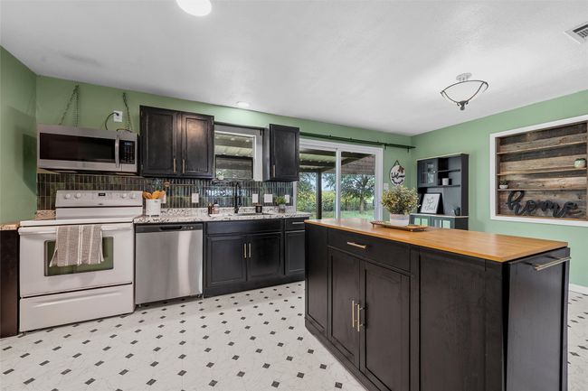 Kitchen featuring stainless steel appliances, wooden counters, backsplash, dark cabinetry, and light floors | Image 11