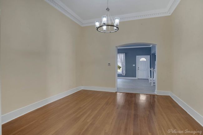 Unfurnished dining area with arched walkways, a chandelier, crown molding, wood finished floors, and a towering ceiling | Image 10