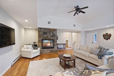 Living room featuring a baseboard heating unit, light hardwood / wood-style floors, vaulted ceiling, a stone fireplace, and ceiling fan | Image 3