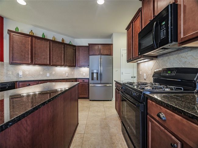Kitchen with black appliances, backsplash, dark stone countertops, light tile patterned floors, and recessed lighting | Image 20