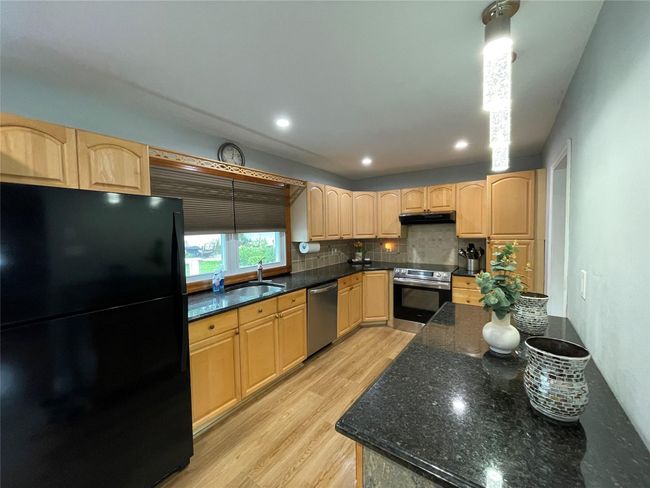Kitchen featuring stainless steel appliances, light brown cabinets, light wood-type flooring, tasteful backsplash, and a sink | Image 15