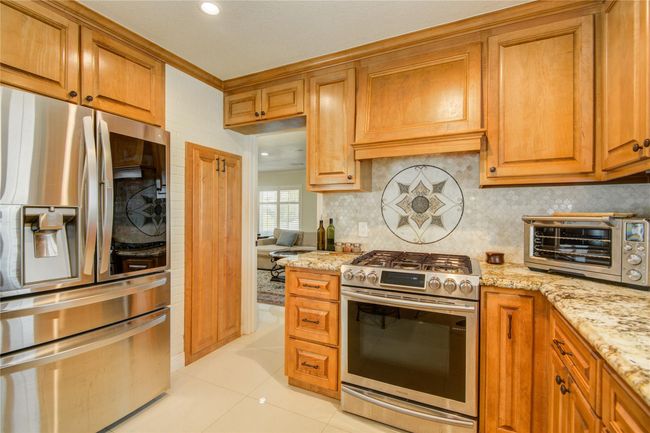 The gas stove and oven are set against a beautifully tiled backsplash, with a peek into the formal living room in the background. | Image 18