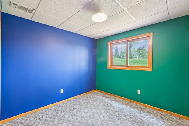 Lower level bedroom with a large window overlooking the side yard and pine trees. | Image 25