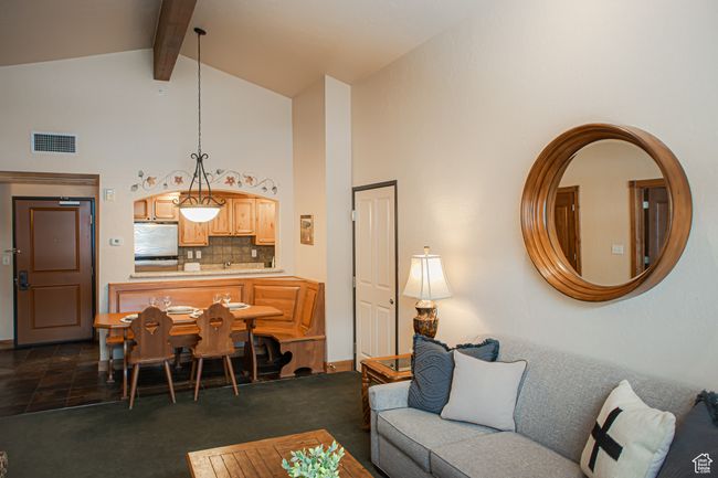 Living room with high vaulted ceiling, visible vents, dark colored carpet, and beam ceiling | Image 5