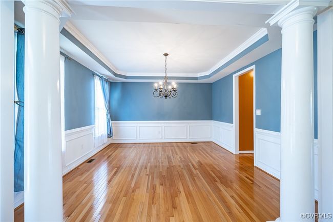 Unfurnished dining area with decorative columns, light wood-type flooring, a tray ceiling, wainscoting, and ornamental molding | Image 6