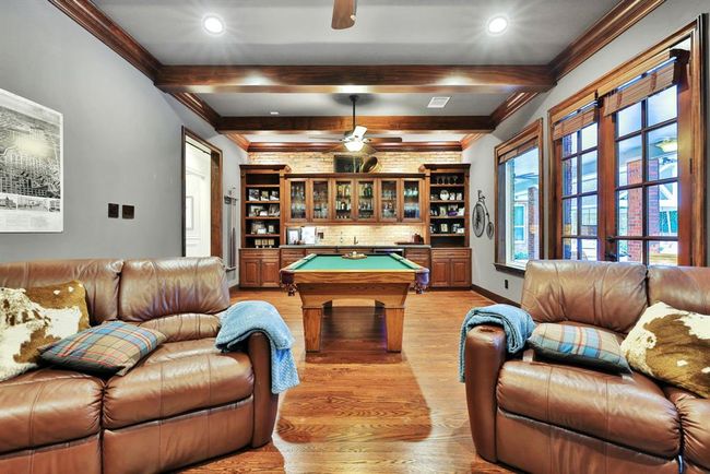 This expansive first-floor game room is a true standout, designed with both functionality and warmth in mind. Custom bookshelves paired with a built-in sink, beverage refrigerator, and glass-front upper cabinets are perfect for entertaining, storing glassware, or showcasing collectibles. | Image 18
