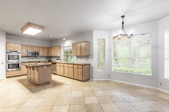 Kitchen featuring appliances with stainless steel finishes, decorative backsplash, light tile patterned flooring, and a kitchen bar | Image 14