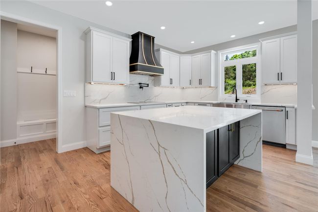 Kitchen featuring light wood-style flooring, wall chimney exhaust hood, high quality fridge, white cabinetry, and built in microwave | Image 12