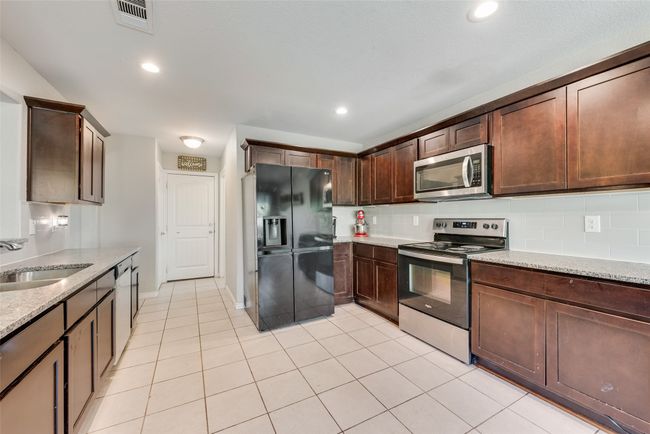 Kitchen featuring appliances with stainless steel finishes, light stone counters, visible vents, decorative backsplash, and a sink | Image 15