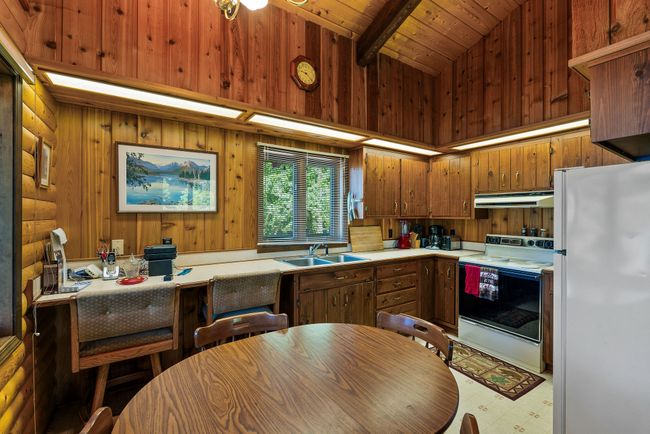 Kitchen with white appliances, under cabinet range hood, light countertops, wooden cabinets, and wooden walls | Image 16
