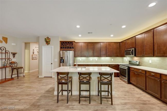 Kitchen with an island with sink, backsplash, a sink, a breakfast bar, and stainless steel appliances | Image 13