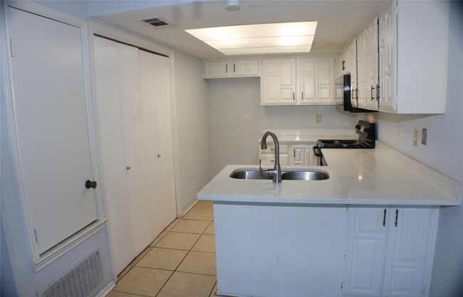 Kitchen with black / electric stove, a peninsula, light tile patterned flooring, and white cabinets | Image 16