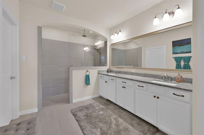 The primary bathroom features a generously sized shower with dual shower heads. The rain head will have you feeling like you're in a spa retreat. Granite countertops, dual sinks, plentiful cabinetry, and stylish fixtures all around... this is the bathroom you deserve! | Image 17