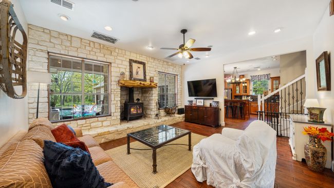 Living area featuring visible vents, a wood stove, ceiling fan with notable chandelier, and wood finished floors | Image 6