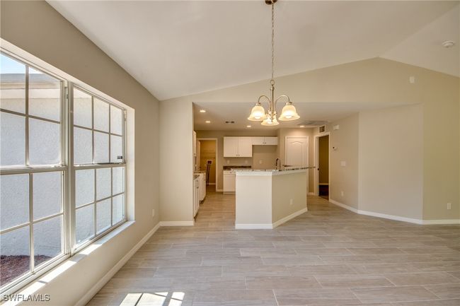 Kitchen with baseboards, white cabinets, decorative light fixtures, vaulted ceiling, and a notable chandelier | Image 13