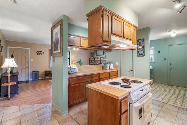 Kitchen featuring white electric stove, under cabinet range hood, light tile patterned flooring, brown cabinetry, and a center island | Image 9