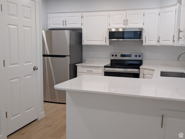 Kitchen with brand new stainless steel appliances, white cabinetry, light countertops, and light wood-style floors | Image 6