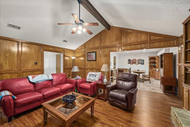 Living room with wood finished floors, a ceiling fan, wooden walls, and a textured ceiling | Image 8