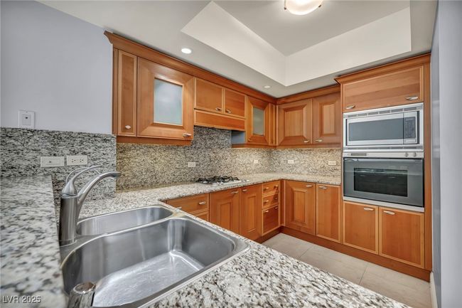 Kitchen with brown cabinets, backsplash, a sink, glass insert cabinets, and appliances with stainless steel finishes | Image 6