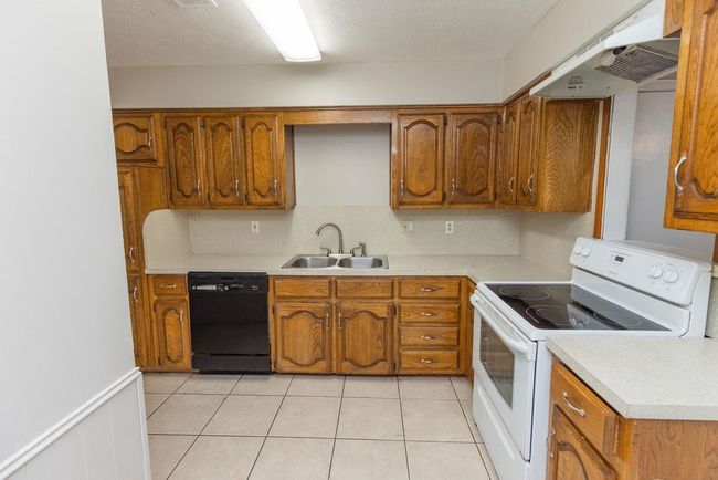 Kitchen with electric stove, dishwasher, a sink, under cabinet range hood, and brown cabinetry | Image 8