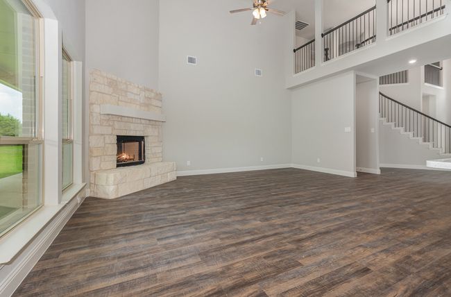 Unfurnished living room with a towering ceiling, a fireplace, wood finished floors, ceiling fan, and stairway | Image 5