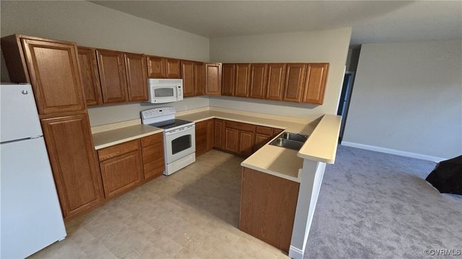 Kitchen with a sink, a peninsula, white appliances, brown cabinets, and light countertops | Image 44