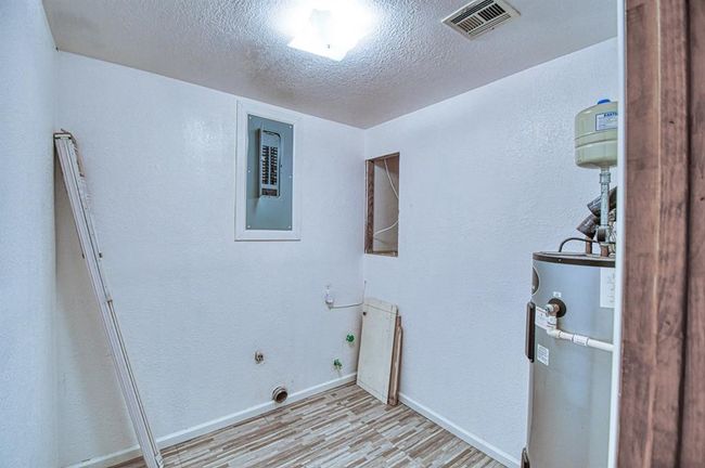 Washroom with water heater, light wood finished floors, a textured ceiling, electric dryer hookup, and baseboards | Image 14