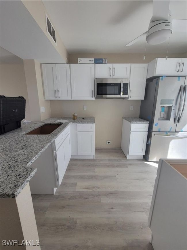 Kitchen featuring refrigerator, a sink, visible vents, white cabinets, and light stone countertops | Image 13