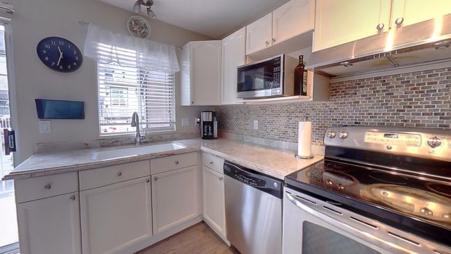 Kitchen with white cabinets, under cabinet range hood, stainless steel appliances, backsplash, and a sink | Image 8