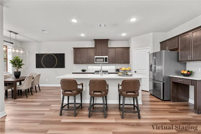 Kitchen with light countertops, dark brown cabinets, decorative backsplash, appliances with stainless steel finishes, and wood finished floors | Image 10
