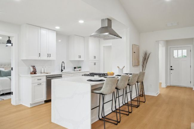 Kitchen with island exhaust hood, a sink, stainless steel appliances, light wood-style floors, and a breakfast bar area | Image 11