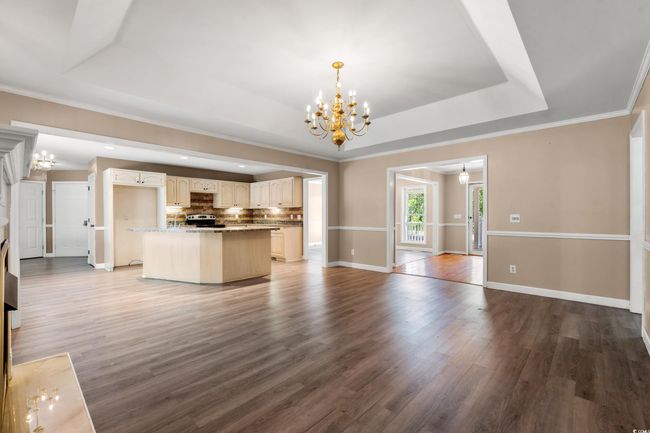Unfurnished living room featuring a chandelier, a raised ceiling, wood finished floors, crown molding, and recessed lighting | Image 27