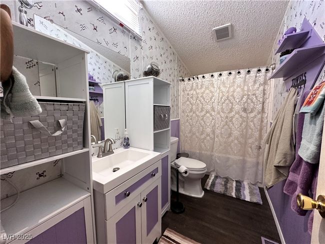 Bathroom with vanity, toilet, a textured ceiling, wallpapered walls, and wood finished floors | Image 12