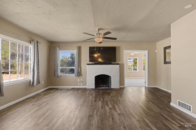 Unfurnished living room with a textured ceiling, wood finished floors, and a fireplace | Image 6
