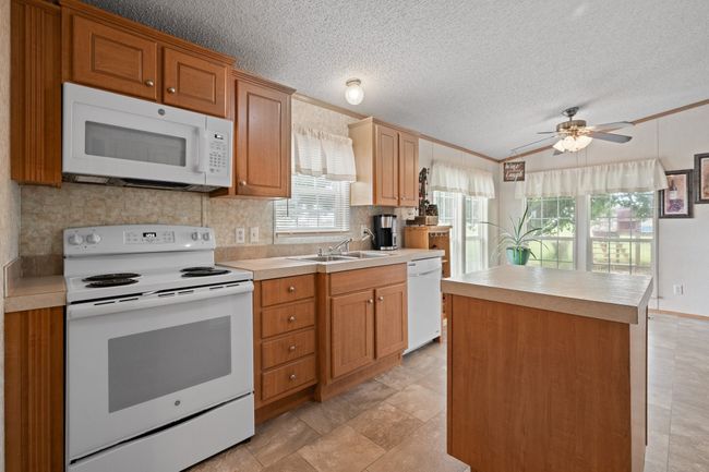 Kitchen with white appliances, backsplash, light countertops, a textured ceiling, and ornamental molding, island and lots of windows which bring in tons of natural light | Image 9