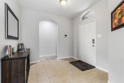 A bright and welcoming entryway with tiled flooring, a high ceiling, and an arched passageway leading to the rest of the home. | Image 3