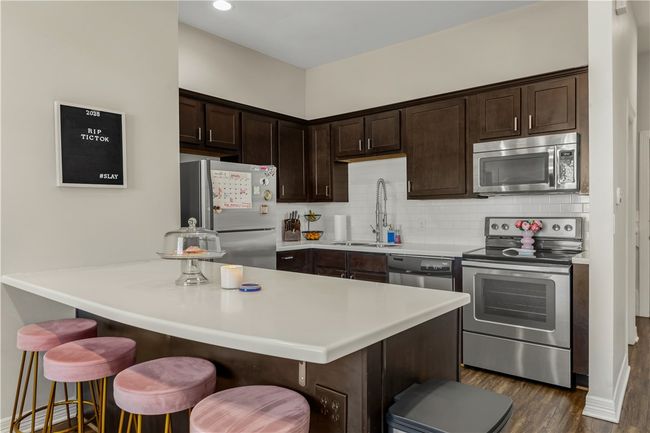 Kitchen featuring sink, appliances with stainless steel finishes, dark brown cabinets, a kitchen breakfast bar, and tasteful backsplash | Image 22