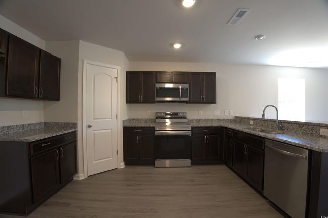 Kitchen featuring appliances with stainless steel finishes, light stone counters, wood finished floors, dark brown cabinets, and recessed lighting | Image 7