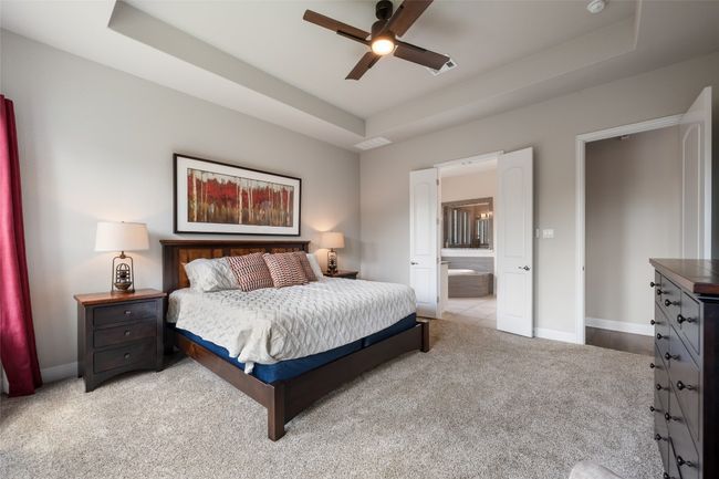 Carpeted bedroom featuring a tray ceiling, ensuite bath, and a ceiling fan | Image 18