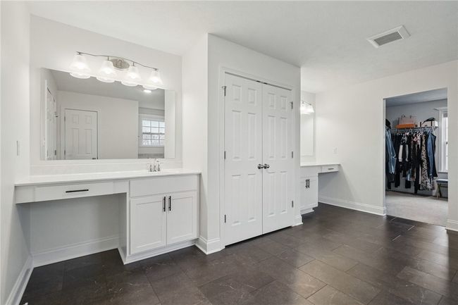 Spacious primary bathroom featuring dual vanities with ample counter space, double linen closet, sleek floor tiles, and crisp white cabinetry. A large walk-in closet is conveniently located just off the bathroom, offering plenty of storage and organization. | Image 22