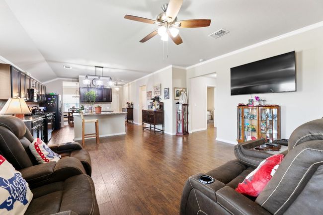 Living room with vaulted ceiling, ornamental molding, dark wood-style floors, visible vents, and a ceiling fan | Image 5