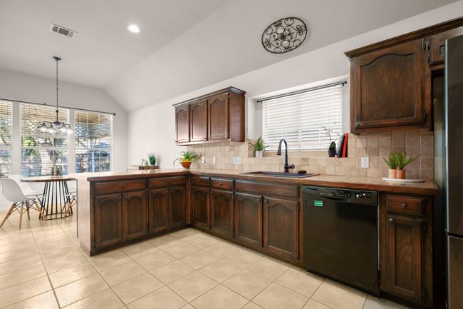 Kitchen featuring lofted ceiling, a peninsula, dark brown cabinets, black dishwasher, and backsplash | Image 17