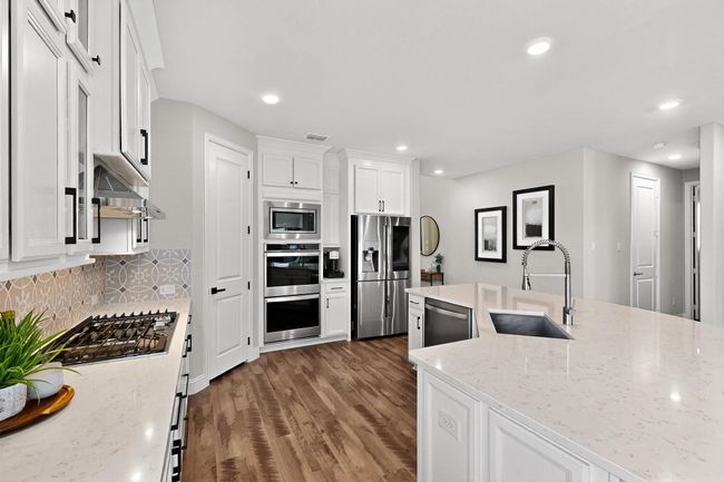 Kitchen featuring white cabinetry, light stone countertops, appliances with stainless steel finishes, dark wood-style flooring, and decorative backsplash | Image 9