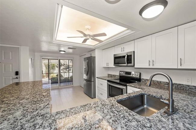 Kitchen featuring stainless steel appliances, dark stone countertops, a tray ceiling, and ceiling fan | Image 10