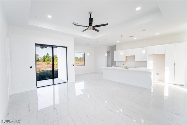 Unfurnished living room with ceiling fan, a tray ceiling, and sink | Image 5