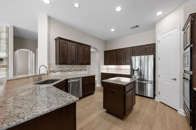 Kitchen featuring stainless steel appliances, arched walkways, a kitchen island, dark brown cabinets, and recessed lighting | Image 7