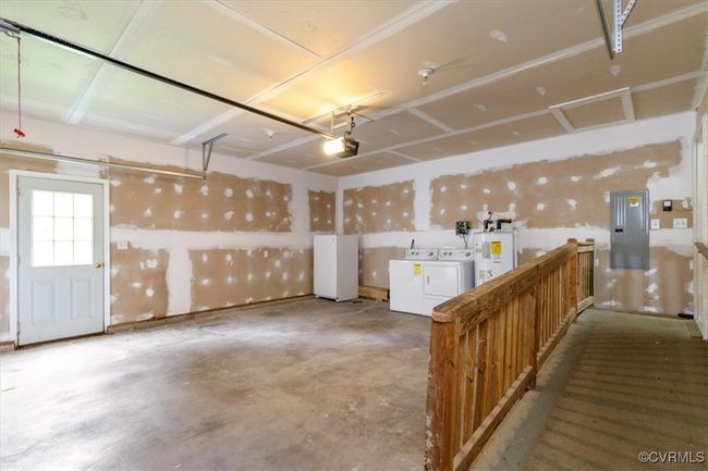 Garage featuring washer and clothes dryer, electric water heater, a garage door opener, freestanding refrigerator, and electric panel | Image 45