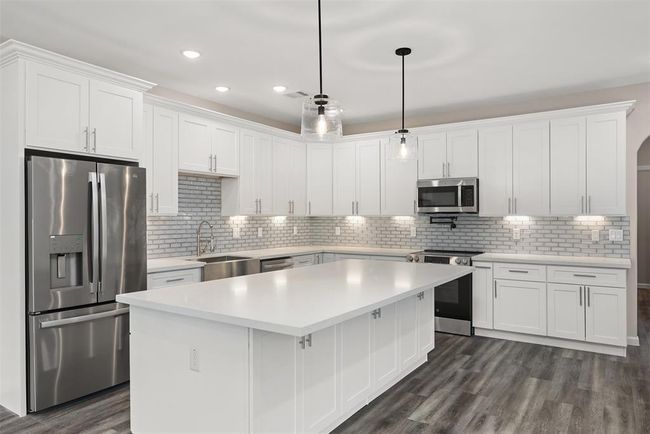 Kitchen with quartz countertops, expertly crafter shaker cabinets, glass tile backsplash, pendant lighting and stainless steel appliances including fridge and wine cooler | Image 6